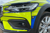 Close-up of the front left side of a bright lime yellow Volvo SUV, showing the headlight, black bumper trim, fog light area, and part of the wheel.